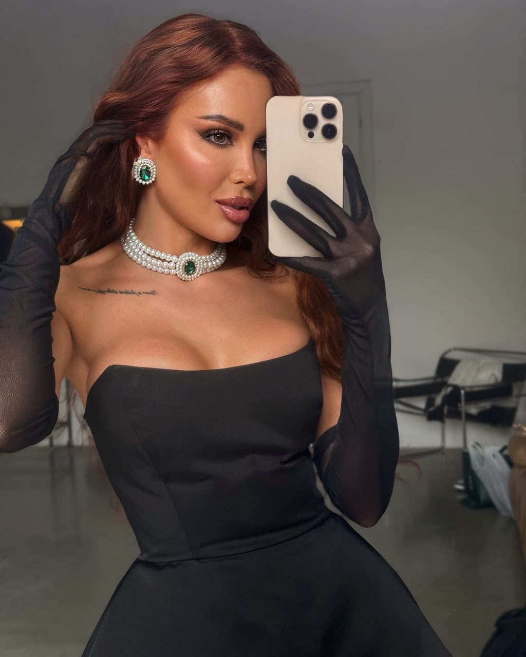 A mirror selfie shows a woman in a black strapless dress and sheer opera gloves, accessorized with a pearl choker and matching earrings.